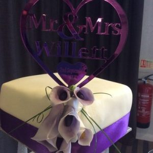 three tier pillared cake white, with purple lillies on one corner, purple ribbon, top tier