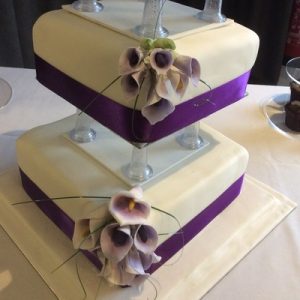 three tier pillared cake white, with purple lillies on one corner, purple ribbon