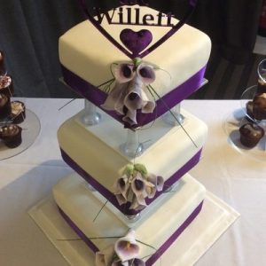 three tier pillared cake white, with purple lillies on one corner, purple ribbon