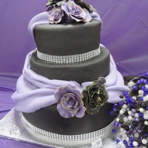 3 tier wedding cake in black and purple with purple swags and purple and black gold edged roses