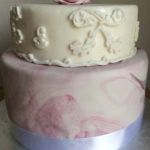 Two tier cake, bottom tier has e a lilac marbled effect, the top tier is all white with moulded scroll designs. Topped with a large lilac shaded flower