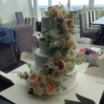4 tier white wedding cake with fresh flower sweeping down from the top layer